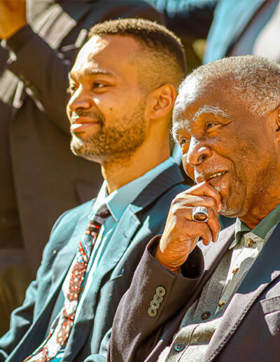 Two men in suits sitting outdoors engaged in conversation during an event