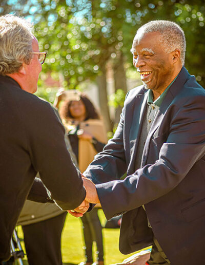 Two men shaking hands warmly at a catered outdoor event, reflecting hospitality and professional event services