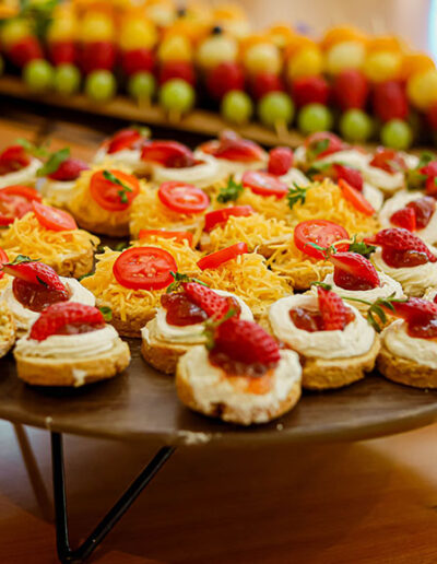 Close-up of assorted mini tarts topped with strawberries, cheese, and cherry tomatoes on a wooden stand.