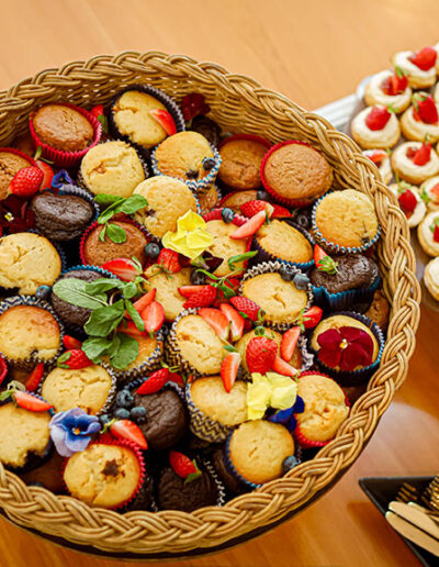 Large woven basket filled with assorted muffins, decorated with fresh berries and edible flowers, perfect for breakfast catering and dessert tables at corporate events
