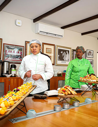 Catering staff in uniform standing behind buffet table with assorted finger foods