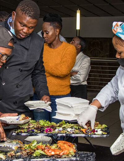 Guests selecting food from a buffet table at an event with catering staff assisting
