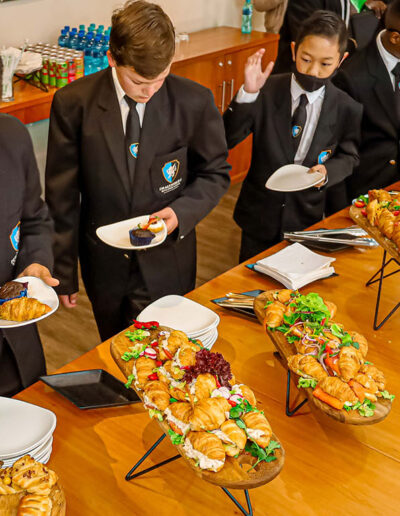 School learners selecting from a spread of gourmet pastries and savoury items, reflecting high-end educational institution catering for formal events
