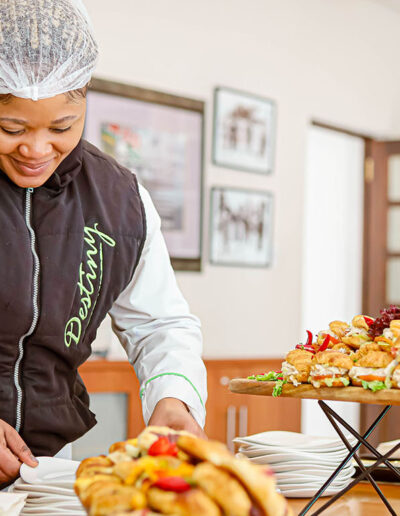 Catering staff member in branded uniform preparing crockery and finger foods for a bespoke indoor catering service